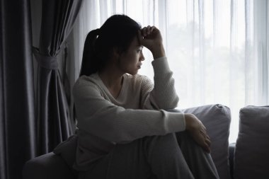 Genç Asyalı kadın evdeki kanepede oturuyor, üzgün, yorgun ve endişeli, akıl sağlığında depresyon geçiriyor. Depresyon, endişe ve uykusuzluk kavramında