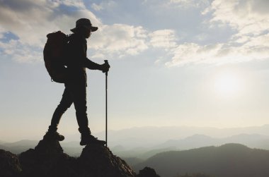Sırt çantalı dağ adamı gün batımında dağlarda yürüyüş yapıyor. Muhteşem bir başarı hikayesi, mücadele, azim ve hırs..