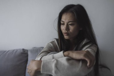 Asyalı genç bir kadının koltukta otururken başı ağrıyor. Çaresiz durum ve stres. Ruh sağlığı konseptinde depresyon sorunu ve endişe krizi.
