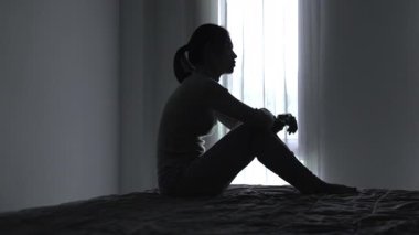 Depresyonda olan kadının silueti yerde oturuyor ve elleri umutsuzca yüzünü örtüyor. Loş bir odada yalnızlık. Akıl sağlığı sorunu kavramı. Uykusuzluk sorunu, görülebilir stres..