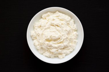 Siyah arka planda beyaz kasede leziz Ricotta peyniri, üst manzara. Yukarıdan, dümdüz uzanmış. 