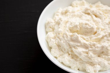 Lezzetli Ricotta Peyniri siyah arka planda, düşük açılı beyaz kasede. Boşluğu kopyala.