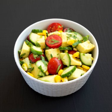 Taze Avokado Domates Salatası, siyah bir yüzey üzerinde bir kasede, yan görünüşte. Yakın plan..