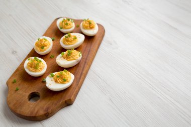 Beyaz ahşap arka planda ve düşük açılı ahşap bir tahtanın üzerinde soğanlı ev yapımı Deviled Eggs. Boşluğu kopyala.