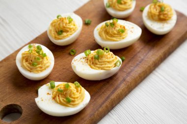 Beyaz ahşap arka planda ve düşük açılı ahşap bir tahtanın üzerinde soğanlı ev yapımı Deviled Eggs. Yakın plan..