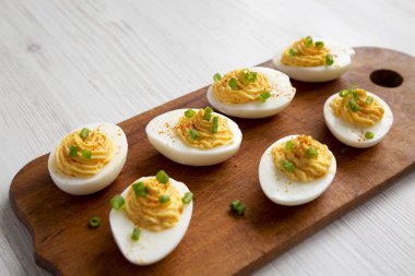 Beyaz ahşap arka planda, sade ahşap bir tahtanın üzerinde soğanlı ev yapımı Deviled Eggs, düşük açılı görüş.. 