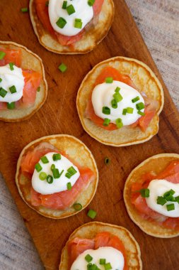 Tütsülenmiş somon, krema ve soğanlı ev yapımı Blini, ahşap bir tahtanın üzerinde. Düz yatıyordu, üstten, yukarıdan..