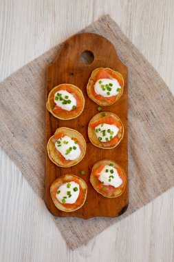 Beyaz ahşap bir yüzey üzerinde füme somon, krema ve soğanlı ev yapımı Blini. Yukarıdan, yukarıdan..