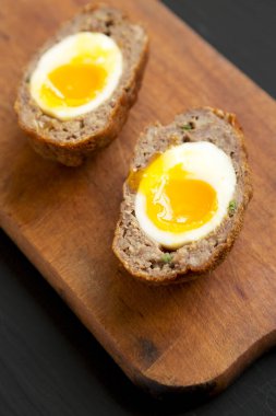 Siyah arka planda, ahşap bir tahtanın üzerinde ev yapımı İskoç yumurtaları. Yakın plan..