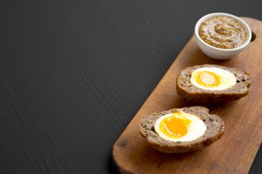 Siyah arka planda, ahşap bir tahtanın üzerinde ev yapımı İskoç yumurtaları. Boşluğu kopyala.