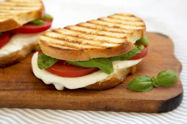 Tasty Grilled Caprese Panini (Mozzarella, Tomatoes and Basil) on a rustic wooden board, side view. Close-up.
