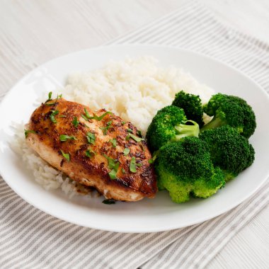 Beyaz ahşap bir masada beyaz bir tabakta ev yapımı tavuk göğsü, pirinç ve brokoli. Yakın plan..