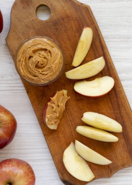 Beyaz ahşap bir masada, üzerinde çiğ kırmızı elmalar ve fındık ezmesi olan ahşap bir tahta. Düz yatıyordu, yukarıdan, yukarıdan..