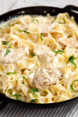 Beyaz ahşap arka planda dökme demir bir tavada ev yapımı Fettuccine Alfredo. Düşük açılı. Yakın plan..
