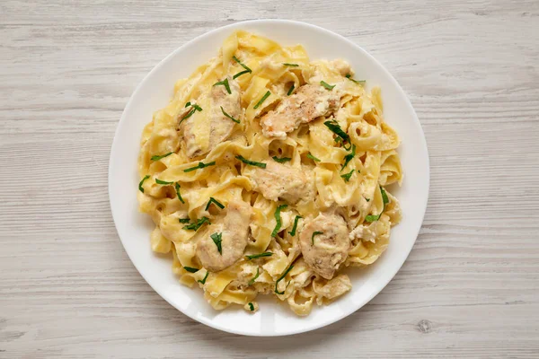 Beyaz ahşap arka planda beyaz bir tabakta ev yapımı Fettuccine Alfredo tavuğu. Dümdüz, tepeden, yukarıdan.