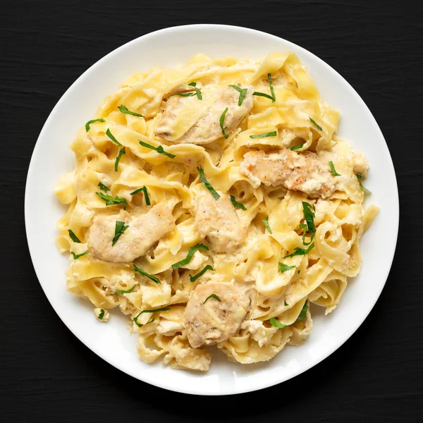 Siyah bir yüzeyde beyaz bir tabakta ev yapımı Fettuccine Alfredo tavuğu. Dümdüz, tepeden, yukarıdan.