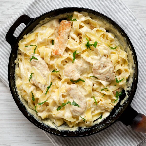 Beyaz ahşap bir masa üzerinde dökme demir bir tavada ev yapımı Fettuccine Alfredo tavuğu. Dümdüz, tepeden, yukarıdan. Yakın plan..