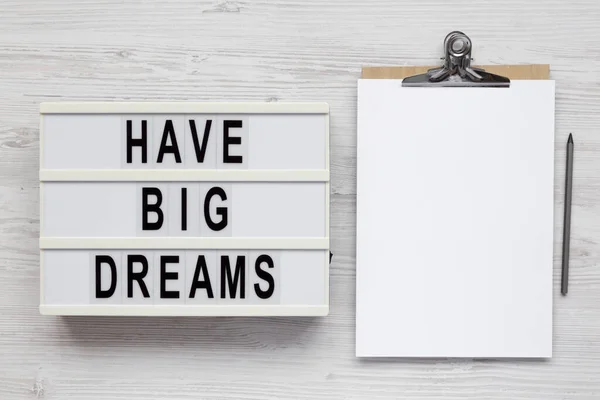 \'Have Big Dreams\' on a lightbox, clipboard with blank sheet of paper on a white wooden background, top view. Flat lay, overhead, from above.