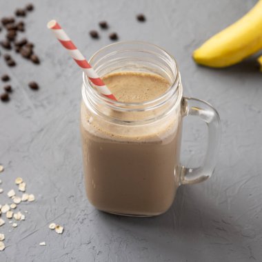 Kahve, yulaf ezmesi ve muzlu ev yapımı smoothie gri arka planda, düşük açılı cam kavanozda. Yakın plan..