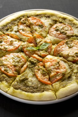Taze domatesli ev yapımı Pesto Pizza ve siyah yüzeyli Mozzarella, düşük açılı. Yakın plan..