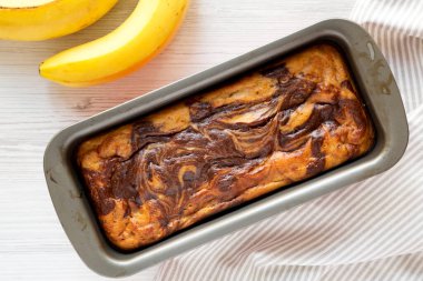 Beyaz ahşap zemin üzerinde ahşap bir tahta üzerinde ev yapımı Muzlu Çikolatalı Ekmek, üst manzara. Dümdüz, tepeden, yukarıdan.