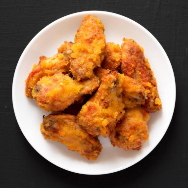 Siyah bir yüzey üzerinde beyaz bir tabakta ev yapımı Baharatlı Tavuk Kanatları. Dümdüz, tepeden, yukarıdan. 