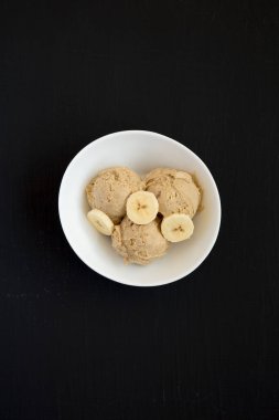 Ev yapımı Fıstık Ezmeli Muzlu Dondurma. Arka planda siyah bir kasede. Dümdüz, tepeden, yukarıdan.
