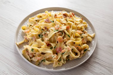 Beyaz ahşap bir masada, düşük açılı bir tabakta ev yapımı sarımsaklı karides pastırmalı Alfredo.. 