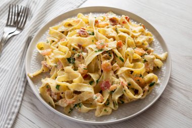 Beyaz ahşap arka planda bir tabakta ev yapımı sarımsaklı karides pastırmalı Alfredo..