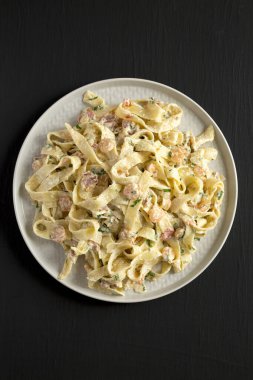 Ev yapımı Sarımsaklı Karides Pastırmalı Alfredo. Siyah arka planda, en iyi manzara. Dümdüz, tepeden, yukarıdan. 