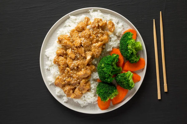 Beyaz pirinçli ev yapımı portakallı tavuk, brokoli ve siyah bir tabakta havuç, üst manzara. Dümdüz, tepeden, yukarıdan.