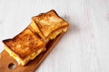 Beyaz ahşap arka planda, ahşap bir tahtanın üzerinde ev yapımı ızgara makarna ve peynirli sandviç. Metin için boşluk.