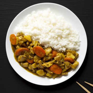 Siyah arka planda beyaz tabakta ev yapımı Japon usulü körili tavuk. Dümdüz, tepeden, yukarıdan. 