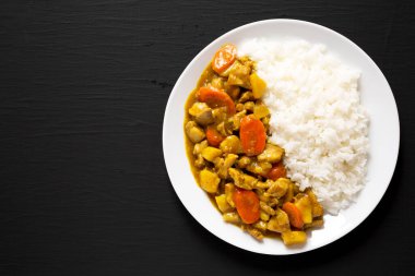 Siyah arka planda beyaz tabakta ev yapımı Japon usulü körili tavuk. Dümdüz, tepeden, yukarıdan. Metin için boşluk.