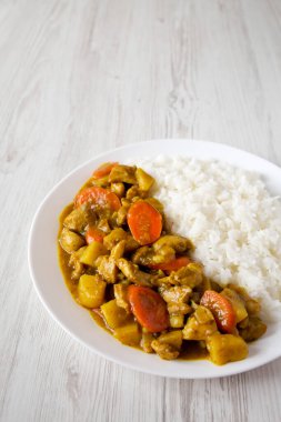 Beyaz ahşap bir yüzey üzerinde beyaz bir tabakta ev yapımı Japon Köri Tavuğu. Metin için boşluk.