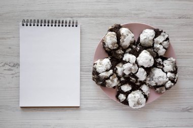 Pembe tabakta ev yapımı çikolatalı kurabiyeler, boş not defteri, üst manzara. Dümdüz, tepeden, yukarıdan. Boşluğu kopyala.