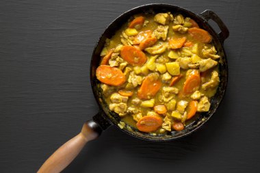 Siyah arka planda dökme demir tavada ev yapımı Japon usulü köri tavuğu. Dümdüz, tepeden, yukarıdan. Boşluğu kopyala.