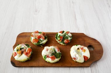 Ev yapımı yumurta beyazı kahvaltı kupaları, yanında ıspanak ve domatesli, ahşap bir tahta tahta, yan görüş. Boşluğu kopyala.