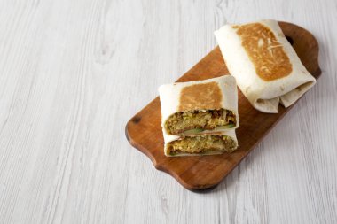 Beyaz ahşap arka planda, ahşap bir tahtanın üzerinde Avocado ve pastırmalı ev yapımı yumurta dürümü. Boşluğu kopyala.