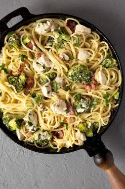 Ev yapımı Tavuk Pastırmalı Brokoli Alfredo gri arka planda dökme demir bir tavada, üst manzara. Dümdüz, tepeden, yukarıdan. Yakın plan..