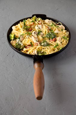 Ev yapımı Tavuk Pastırmalı Brokoli Alfredo gri arka planda dökme demir bir tavada, yan manzara. 