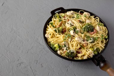 Ev yapımı Tavuk Pastırmalı Brokoli Alfredo gri bir yüzey üzerinde dökme demir bir tavada, yan görüş. Boşluğu kopyala.