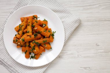 Beyaz ahşap bir yüzey üzerinde beyaz bir tabakta otlu ev yapımı kızarmış havuç, üst manzara. Dümdüz, tepeden, yukarıdan. Boşluğu kopyala.