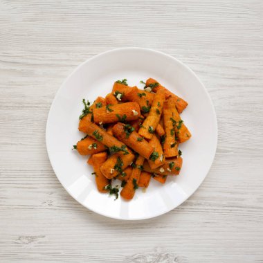 Beyaz ahşap bir yüzey üzerinde beyaz bir tabakta otlu ev yapımı kızarmış havuç, üst manzara. Dümdüz, tepeden, yukarıdan. 