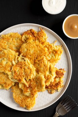 Homemade Potato Pancakes Latkes with Apple Sauce and Sour Cream on a black wooden surface, top view. Flat lay, overhead, from above. 