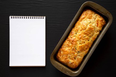 Ev yapımı peynirli ekmek, siyah arka planda boş not defteri, üst manzara. Dümdüz, tepeden, yukarıdan. 