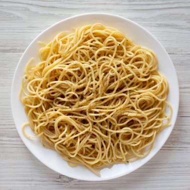 Pecorino Romano ve Pepper 'lı ev yapımı Cacio E Pepe Pasta beyaz bir tabakta beyaz ahşap arka planda, üst manzara. Yukarıdan, yukarıdan, dümdüz.