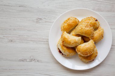 Beyaz ahşap arka planda beyaz bir tabakta el yapımı vişneli turtalar. Üst manzara, yukarıdan, düz yatıyordu. Boşluğu kopyala.