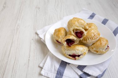 Beyaz ahşap arka planda beyaz bir tabakta el yapımı vişneli turtalar. Boşluğu kopyala.