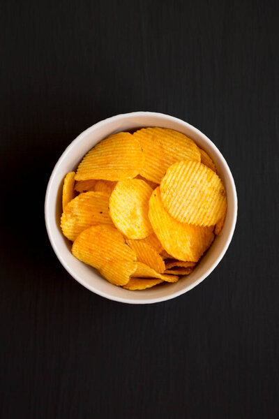 Сырные картофельные чипсы в миске на черной поверхности, вид сверху. Плоский лежал, сверху, сверху.